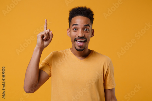 Excited young african american guy in casual t-shirt posing isolated on yellow orange background in studio. People lifestyle concept. Mock up copy space. Holding index finger up with great new idea.