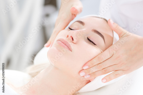Close-up of cosmetologist's hands doing facial massage to beautiful young caucasian female client to rejuvenate and restore skin elasticity. Spa treatment concept