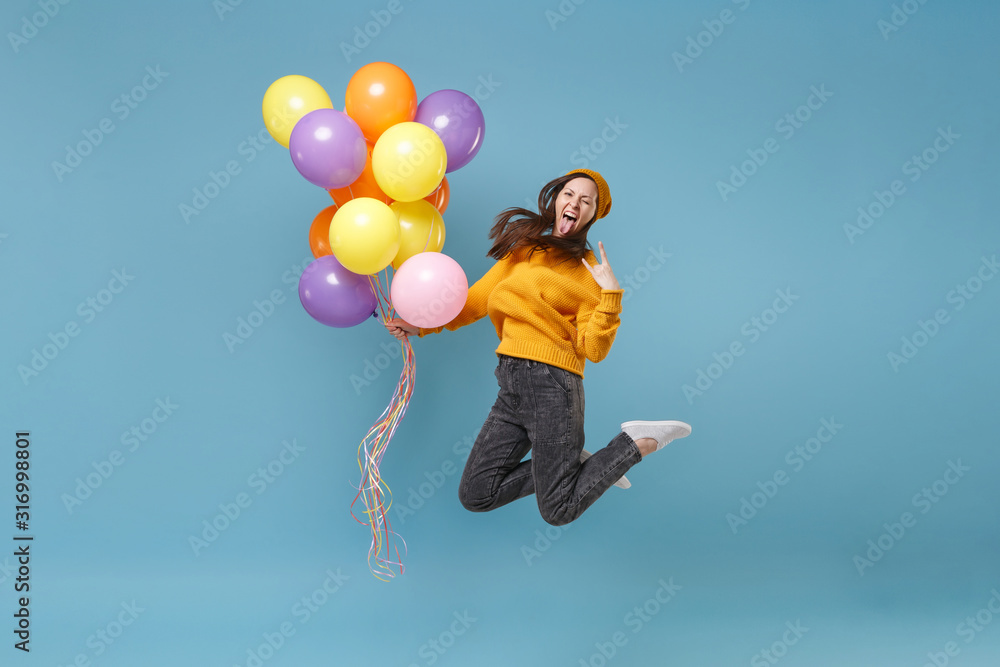 Surprised woman in sweater hat posing isolated on blue background. Birthday holiday party, people emotions concept. Mock up copy space. Celebrating hold air balloons jumping showing horns up gesture. Surprised woman in sweater hat posing isolated on blue background. Birthday holiday party, people emotions concept. Mock up copy space. Celebrating hold air balloons jumping showing horns up gesture.