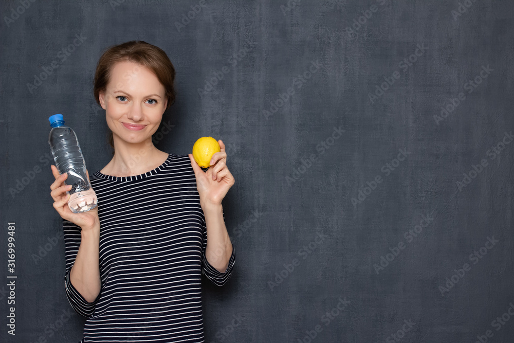 Portrait of happy young woman holding lemon and bottle of water Portrait of happy young woman holding lemon and bottle of water