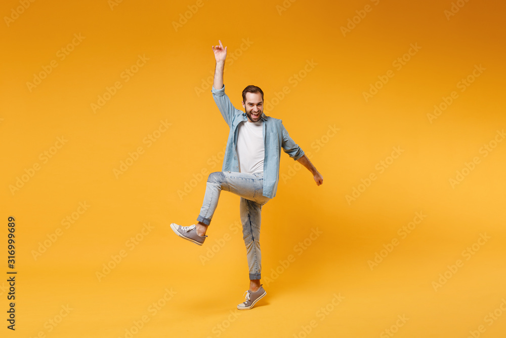 Cheerful young bearded man in casual blue shirt posing isolated on yellow orange background studio portrait. People emotions lifestyle concept. Mock up copy space. Jumping, pointing index finger up.