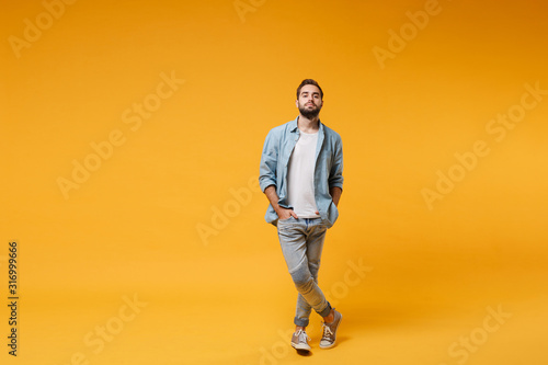 Vászonkép Handsome young bearded man in casual blue shirt posing isolated on yellow orange background, studio portrait
