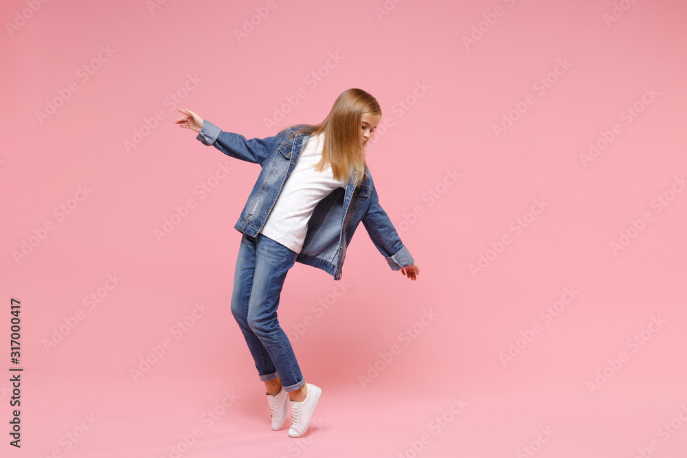 Little blonde kid girl 12-13 years old in denim jacket isolated on pastel pink wall background children studio portrait. Childhood lifestyle concept. Mock up copy space. Standing on toes, dancing. Little blonde kid girl 12-13 years old in denim jacket isolated on pastel pink wall background children studio portrait. Childhood lifestyle concept. Mock up copy space. Standing on toes, dancing.