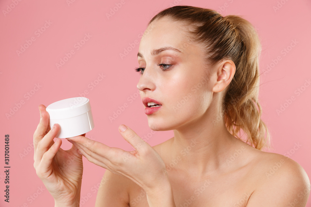 Close up blonde half naked woman 20s perfect skin nude makeup blue eyes isolated on pastel pink wall background. Skin care healthcare procedures concept Apply moisturizer, facial cream from container. Close up blonde half naked woman 20s perfect skin nude makeup blue eyes isolated on pastel pink wall background. Skin care healthcare procedures concept Apply moisturizer, facial cream from container.