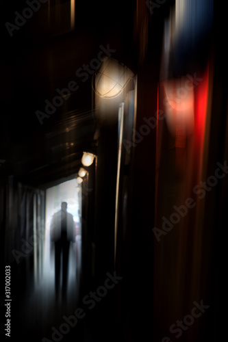 Silhouette of a man in a coat in a dark alley on a rainy night. theme of violence offense and cruelty. blur effect