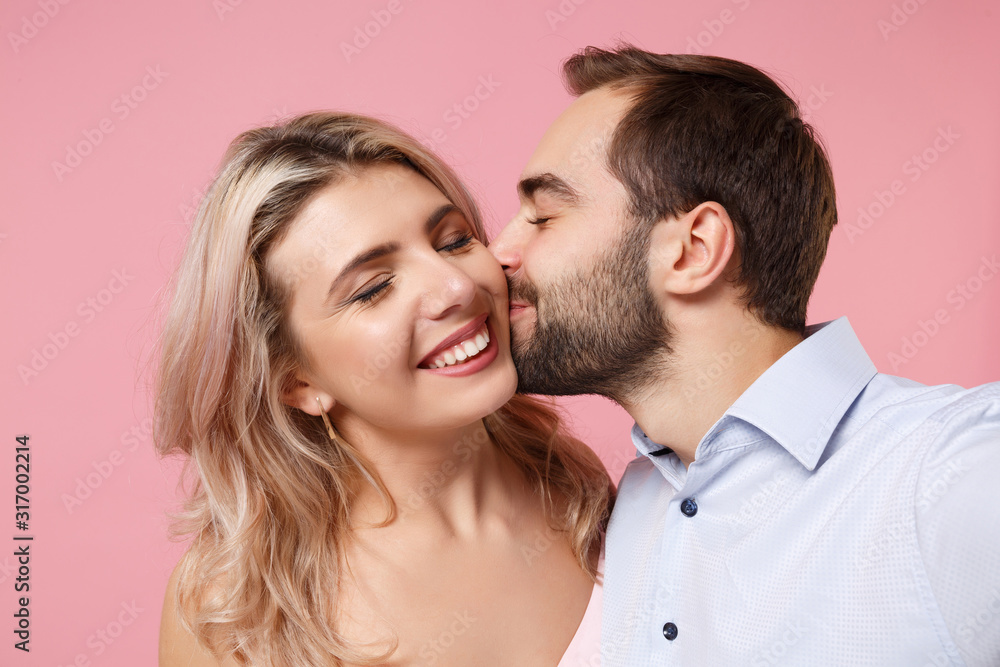 Close up of couple two guy girl in party outfit posing isolated on pastel pink background. Valentine's Day Women's Day birthday holiday concept. Kissing in cheeks doing selfie shot on mobile phone. Close up of couple two guy girl in party outfit posing isolated on pastel pink background. Valentine's Day Women's Day birthday holiday concept. Kissing in cheeks doing selfie shot on mobile phone.