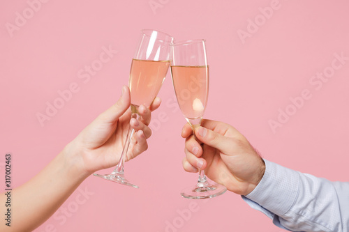 Close up cropped photo of female, male hold in hands glass of champagne isolated on pastel pink background Fototapeta