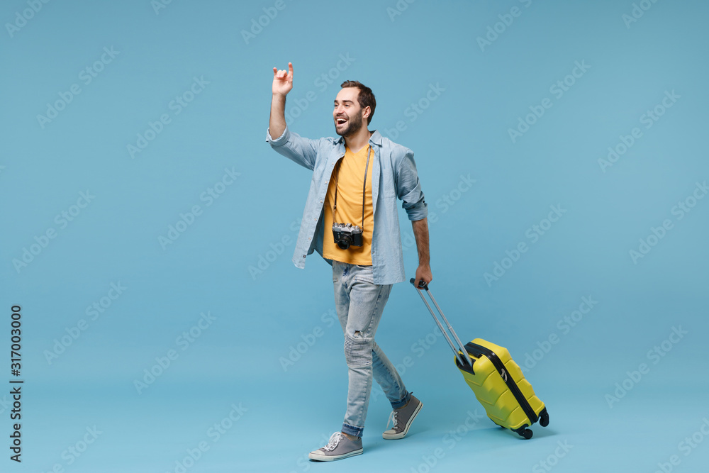 Funny traveler tourist man in yellow clothes with photo camera isolated on  blue background. Male passenger traveling on weekends. Air flight journey.  Hold suitcase waving hand for greeting catch taxi. Stock Photo |