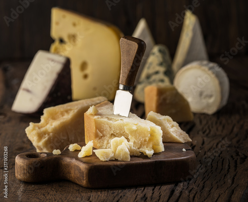 Piece of Parmesan cheese  on the wooden board. Assortment of different cheeses at the background.