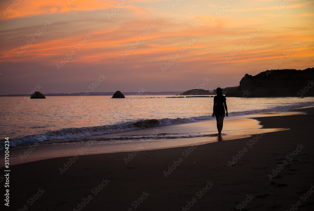 Portugal, Algarve, The best beaches of Portimao, Praia da Rocha, lilac golden sunset over the waves of The Atlantic Ocean, a girl walking the waves, silhouette happy woman at sunset on the beach