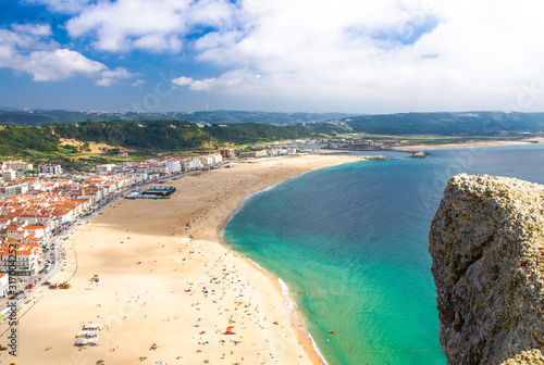 Portugal, panoramic view of Nazare in summer, mountain landscape with dense greenery in the background, Nazare coastline with white sand and blue azure water of the Atlantic Ocean, harbor Nazare