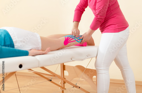 Physical therapist applying kinesio tape on female patient's leg. Kinesiology, physical therapy, rehabilitation concept.