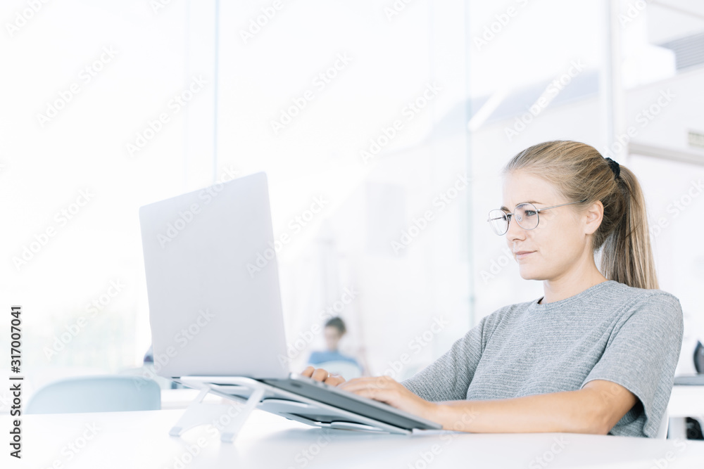 Profile of a blonde girl working with a laptop in a coworking and people around Profile of a blonde girl working with a laptop in a coworking and people around