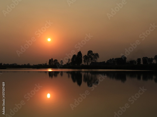  silhouette tree in asia with sunset.Tree silhouetted against a setting sun.Dark tree on open field dramatic sunrise and reflection in water.