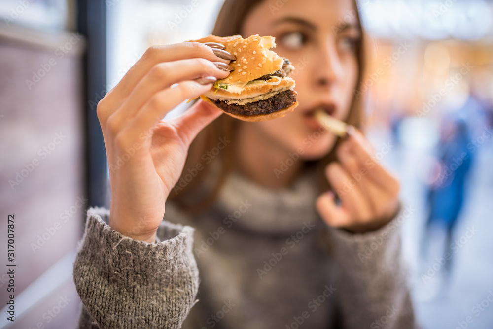 Beautiful young girl eats fast food hamburger in a cafe. Beautiful young girl eats fast food hamburger in a cafe.