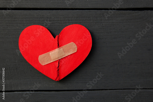 Two parts of red broken wooden heart taped by a patch. Concept of the forgiveness, renewal of relations and healing