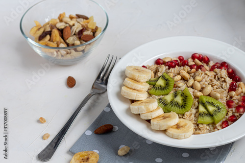 Breakfast consisting of oatmeal, nuts and fruits. Kiwi, banana, pomegranate and almonds decorate the plate. Healthy food, on a white background.