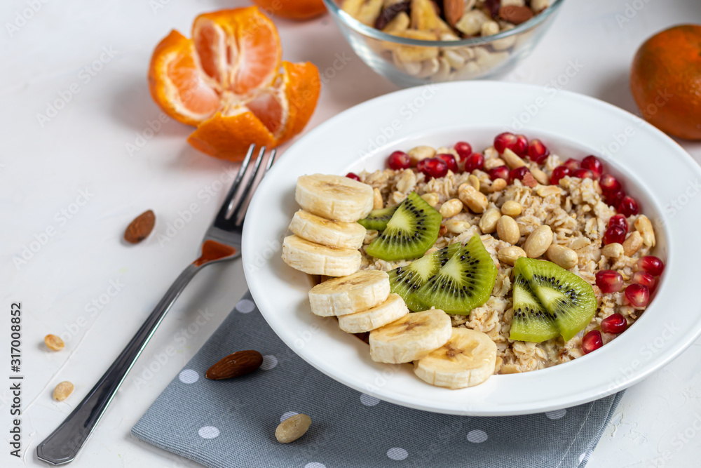 Breakfast consisting of oatmeal, nuts and fruits. Kiwi, banana, pomegranate and almonds decorate the plate. Healthy food, on a white background. Breakfast consisting of oatmeal, nuts and fruits. Kiwi, banana, pomegranate and almonds decorate the plate. Healthy food, on a white background.
