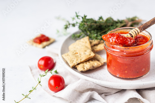 Ajvar (pepper mousse) or pindjur red vegetable spread made from paprika and tomatoes in glass jar on light stone table. Serbian native food.