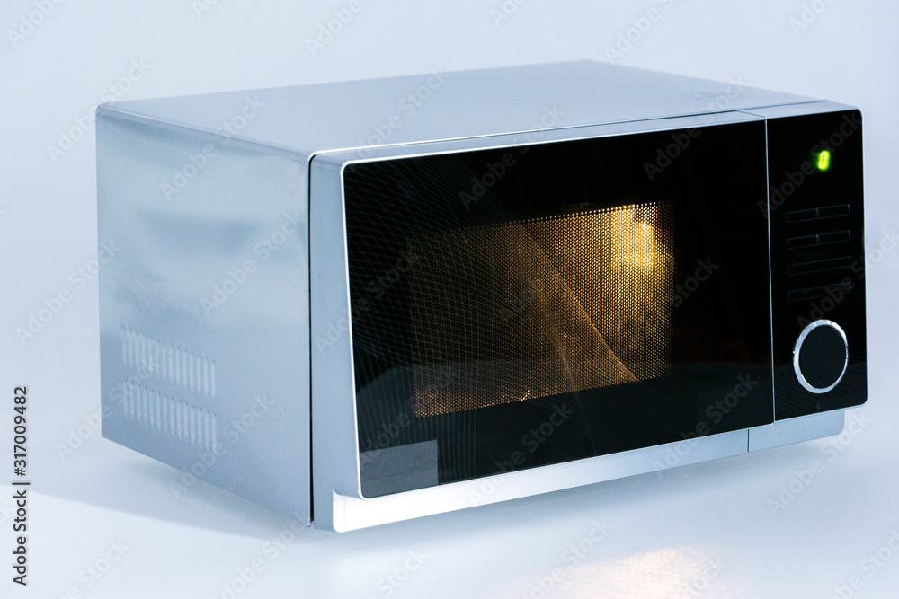 Obraz premium metal and electrical microwave oven with light on white background