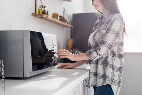 cropped view of woman in shirt using microwave in kitchen photo