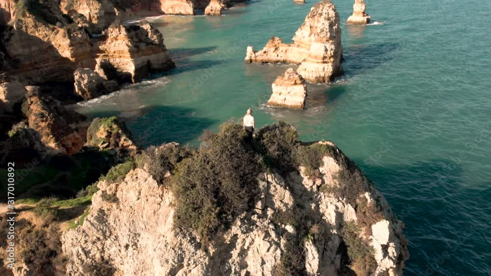 AERIAL: Girl is standing on the cliffs in Portugal enjoying a beautiful view AERIAL: Girl is standing on the cliffs in Portugal enjoying a beautiful view