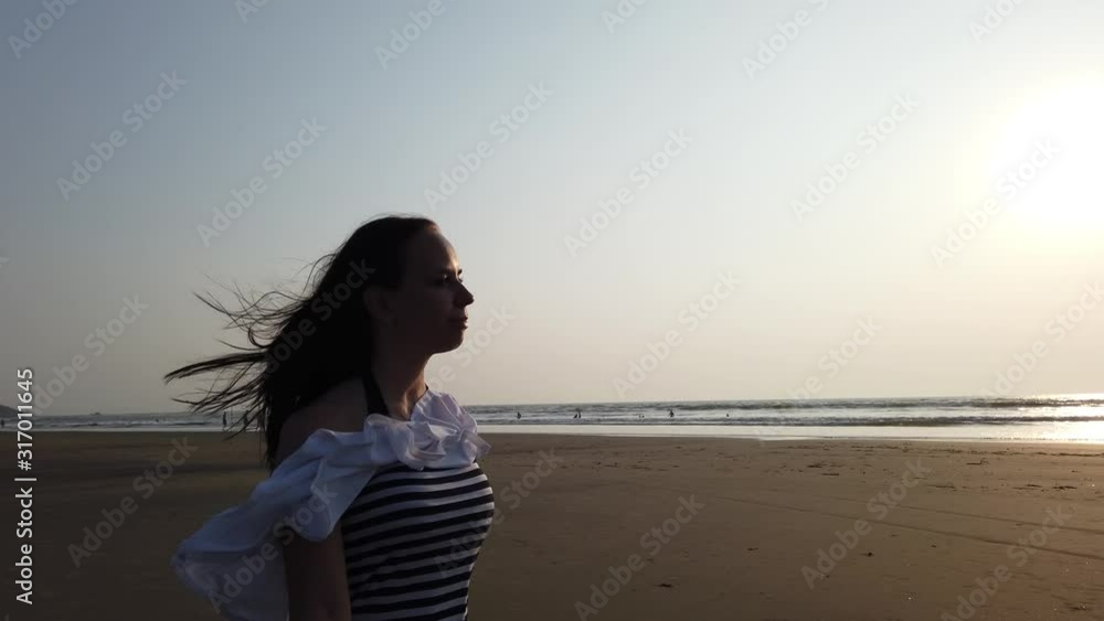 Young slim beautiful woman on sunset beach. Woman walking on beach under sunset light Young slim beautiful woman on sunset beach. Woman walking on beach under sunset light