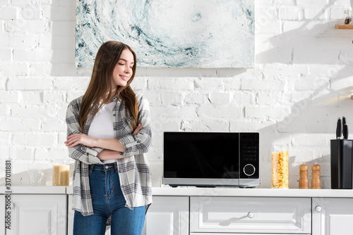 smiling and attractive woman standing near microwave in kitchen