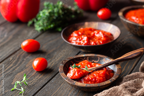 Ajvar (pepper mousse) or pindjur red vegetable spread made from paprika and tomatoes in wooden bowl on the rustic wooden table. Serbian native food. photo