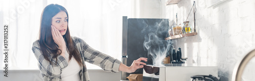 Fotografie panoramic shot of scared and attractive woman looking at broken microwave in kit