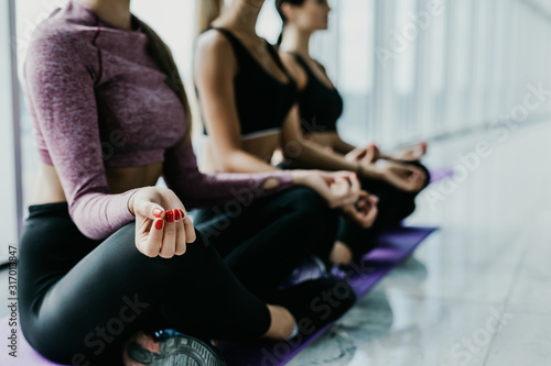 Three young women meditating in lotus pose during yoga class in health club. Young three Women sitting on floor near window with city view