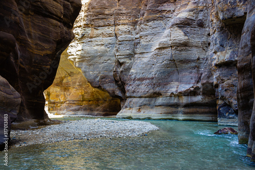 Wadi Mujib Nature Reserve in Jordan. Mujib Canyon near Dead Sea coastline. River flows between sheer cliffs of canyon. Colorful rocks go vertically up.