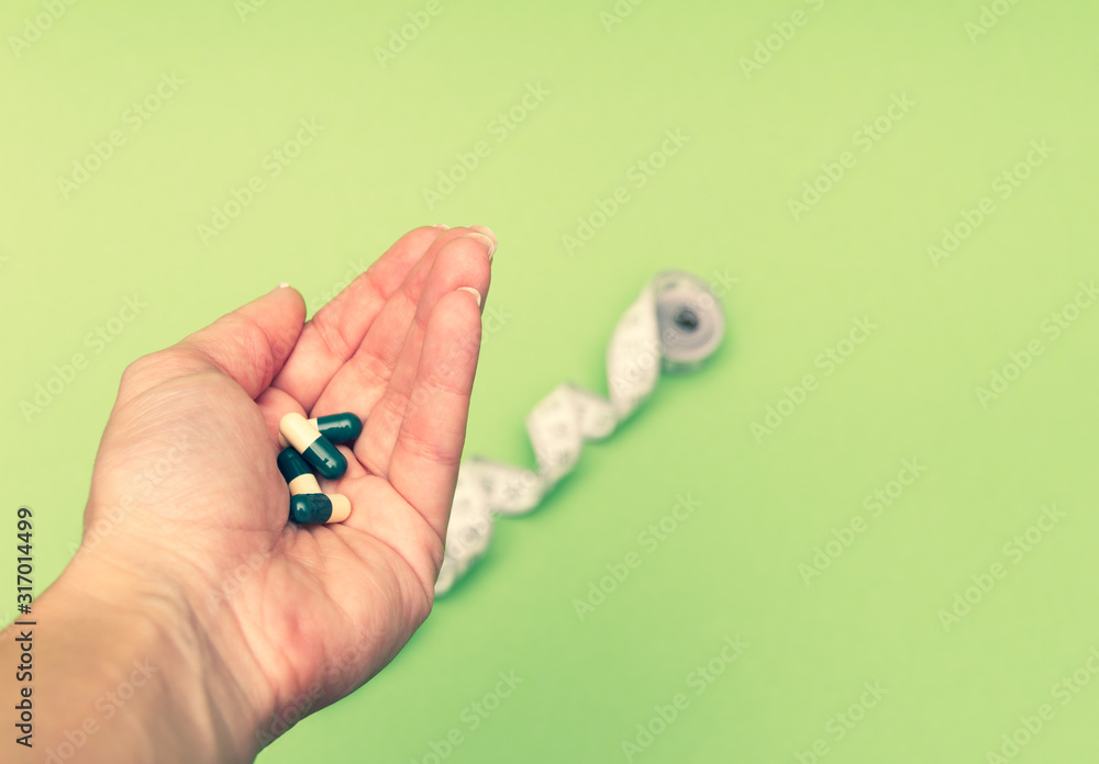Diet pills in woman's hand and measuring meter on green background. Losing weight concept. Diet pills in woman's hand and measuring meter on green background. Losing weight concept.