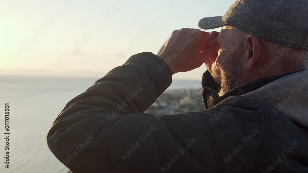 Senior traveler making binocular gesture and looking landscape sitting on a hill Senior traveler making binocular gesture and looking landscape sitting on a hill