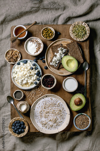 Healthy breakfast. Variety of breakfast dishes wheat, yogurt, kefir, cottage cheese, avocado, rye bread, seeds, nuts and berries assortment in ceramic bowls. Wooden and textile background. Flat lay