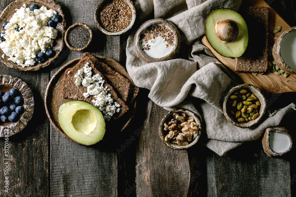 Healthy breakfast. Variety of breakfast dishes sprouted wheat, yogurt, kefir, cottage cheese, avocado, rye bread, seeds, nuts and berries assortment in ceramic bowls over wooden background. Flat lay Healthy breakfast. Variety of breakfast dishes sprouted wheat, yogurt, kefir, cottage cheese, avocado, rye bread, seeds, nuts and berries assortment in ceramic bowls over wooden background. Flat lay