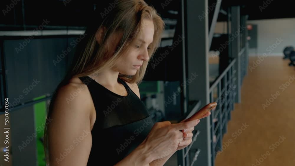 fit slim hipster millenial woman standing in the gym using phone after workout. female rest, relax, chats, browsing internet in sport center. business, break, busy concept fit slim hipster millenial woman standing in the gym using phone after workout. female rest, relax, chats, browsing internet in sport center. business, break, busy concept