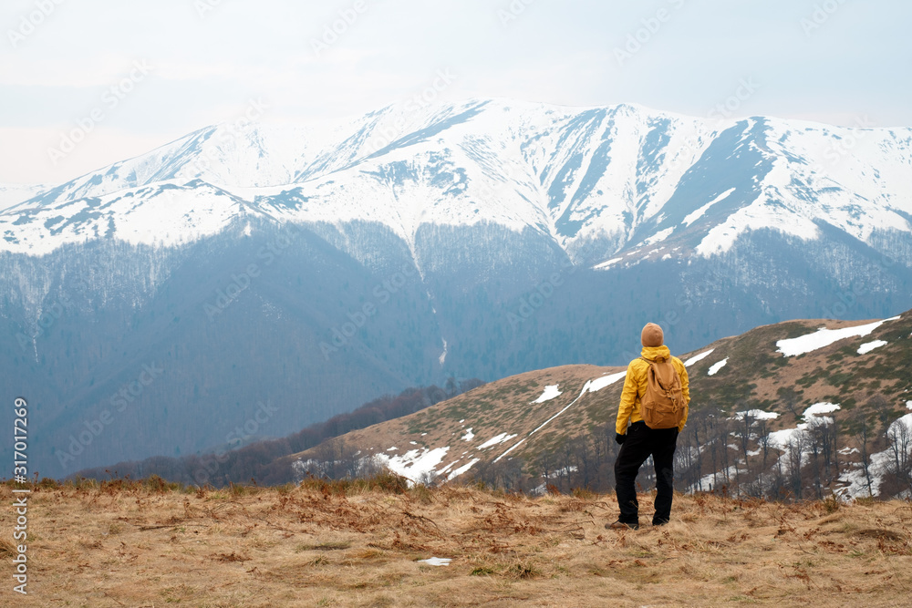 Man in yellow jacket with backpack in spring snowy mountains. Travel concept. Landscape photography