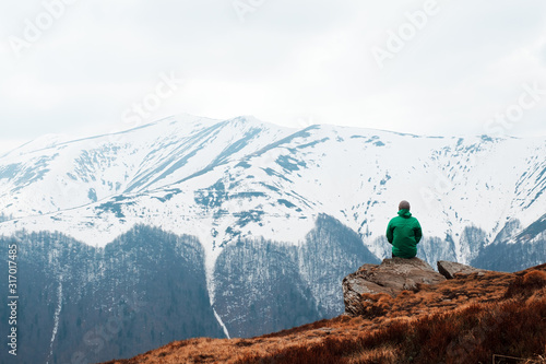 Man in green jacket sitting on rock in spring mountains. Travel concept. Landscape photography