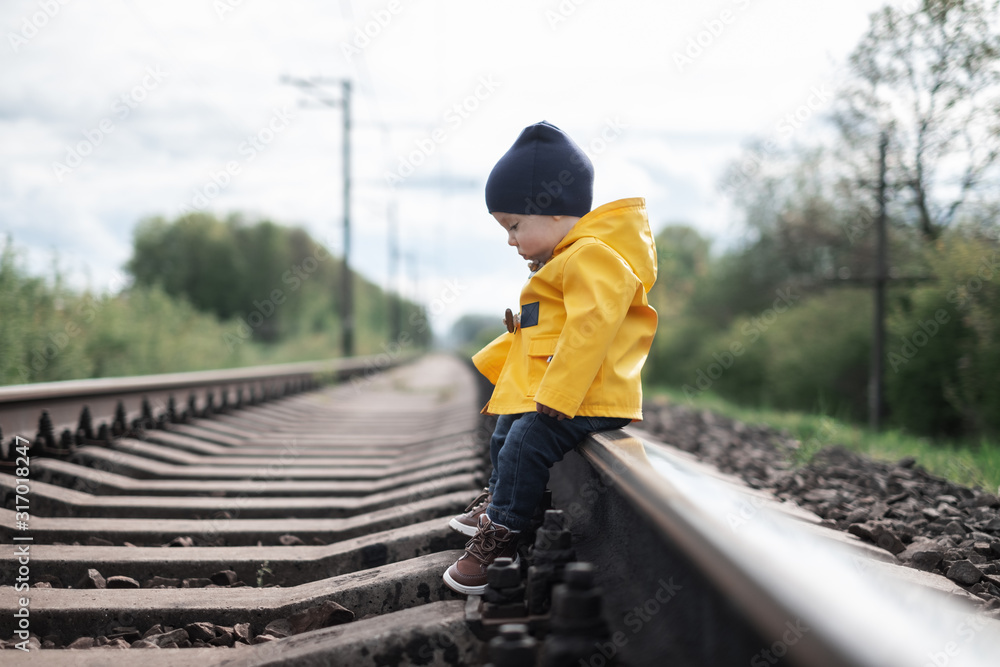Kid in yellow jacket sitting on railroad
