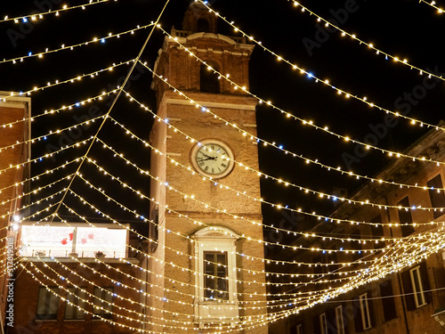 Ferrara, Italy. The clock tower illuminated with Christmas lights.
