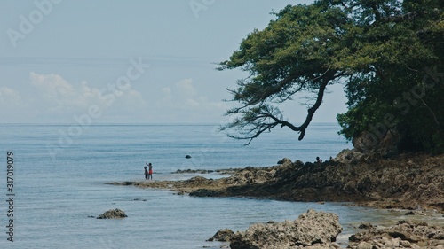 Melsisi, Pentecost Island / Vanuatu - May 10 2019: beautiful cinematic seascape at the remote southern pacific tropical island rocky shore and lush trees while local kids playing on the beach photo