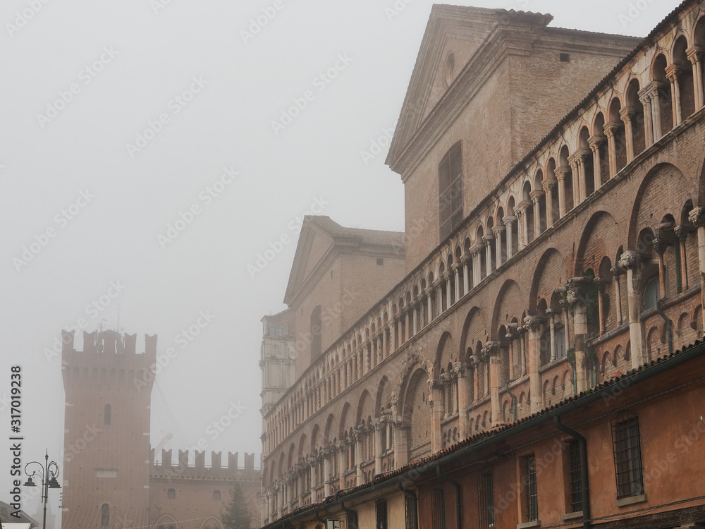 Ferrara, Italy. Main square, Torre della Vittoria and Loggia dei Merciai, foggy winter morning.