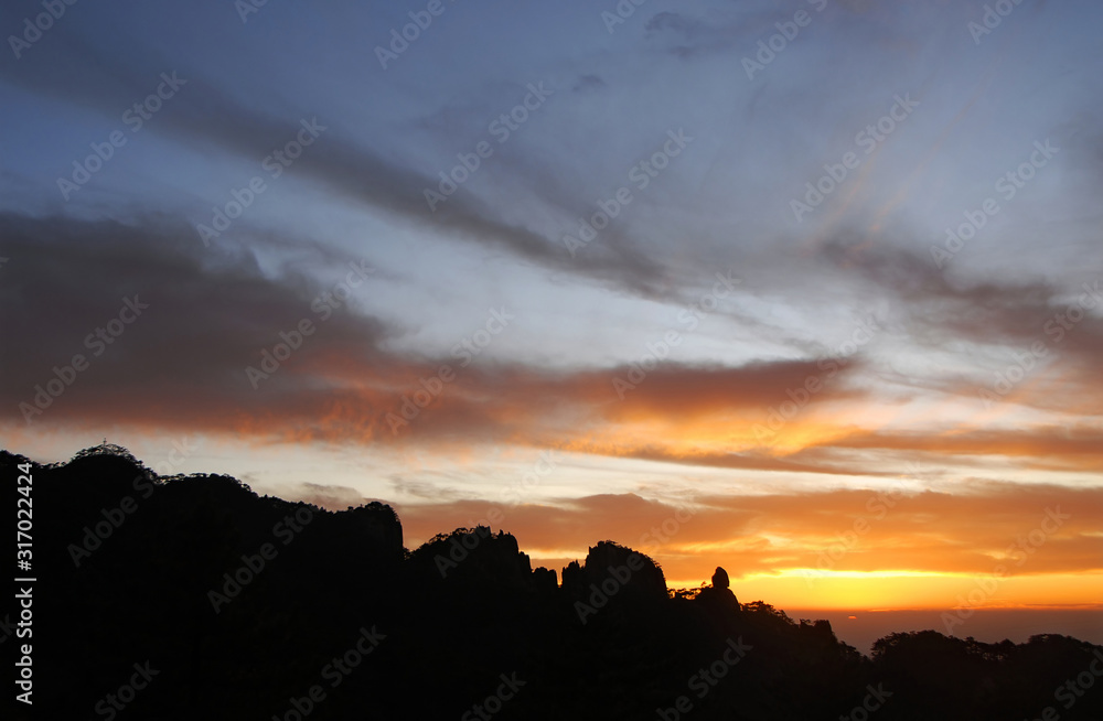 Huangshan Mountain in Anhui Province, China. Sunset over Huangshan with colorful sky and clouds and a silhouette of the mountain. Sun nearly set. Sunset near the summit of Huangshan Mountain, China.