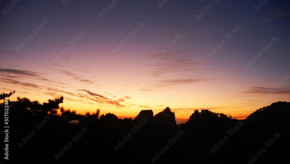 Huangshan Mountain in Anhui Province, China. View after sunset on Huangshan with a colorful purple sky, clouds and a silhouette of the mountain. Sunset near the summit of Huangshan Mountain, China.