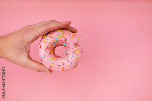 Canvas Print Female hand holding delicious donut on pink background, closeup