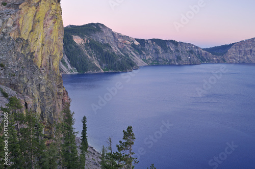 Landscape of the shoreline of Crater Lake National Park at twilight with conifers and blue waters  Oregon  USA