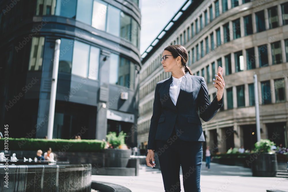 Smartly dressed businesswoman looking away from phone and standing on street Smartly dressed businesswoman looking away from phone and standing on street