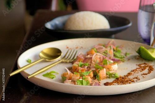 Asian cuisine. Diced raw salmon with red onions, lemon and mint, with steamed rice on the side. Close up shot.