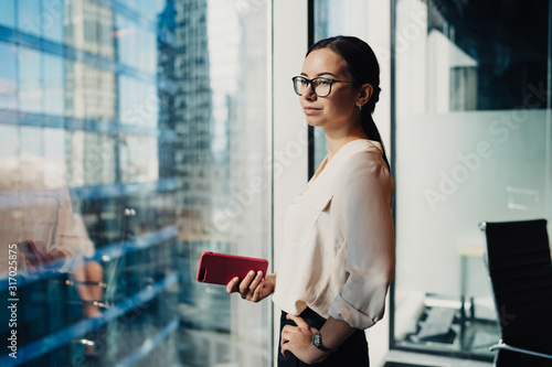 Businesswoman with smartphone in hand looking at window